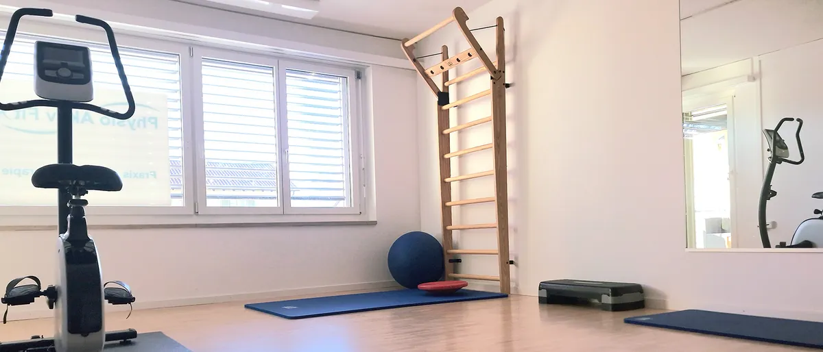 Trainingsraum der Praxis mit Ergometer, Sprossenwand, Gymnastikball und Matten auf Parkettboden