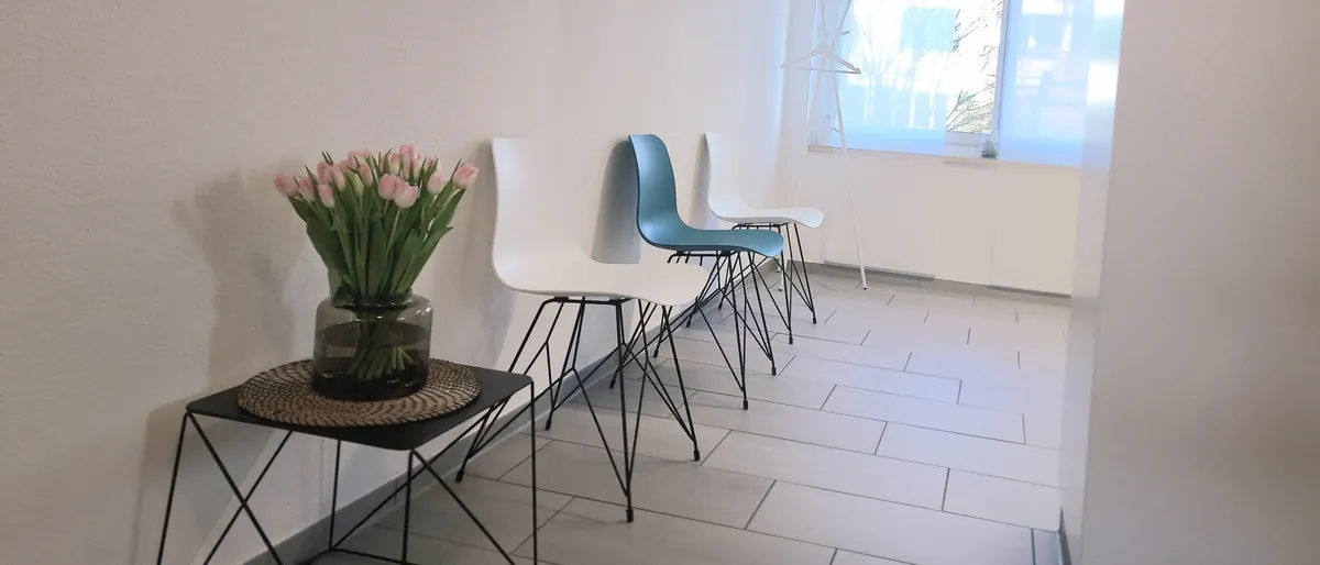 Helle Wartezone der Praxis mit weissen und türkisen Stühlen, Tulpen auf einem Beistelltisch und grossem Fenster